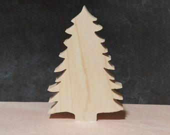 May include: A wooden cutout of a Christmas tree in a light brown color. The tree is standing on a pink surface.