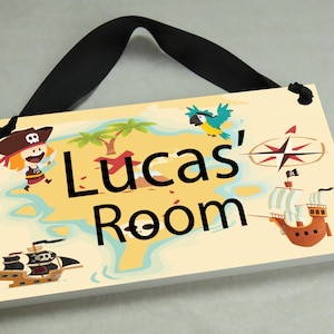 May include: A wooden sign with a pirate theme, featuring a cartoon pirate, a parrot, a ship, and a compass. The sign reads "Lucas' Room".