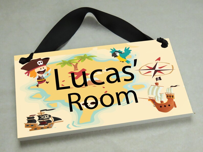 May include: A wooden sign with a pirate theme, featuring a cartoon pirate, a parrot, a ship, and a compass. The sign reads "Lucas' Room".