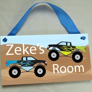 May include: A blue and brown wooden door sign with the text "Zeke's Room" and two monster truck illustrations. The trucks are black with yellow and blue flames.