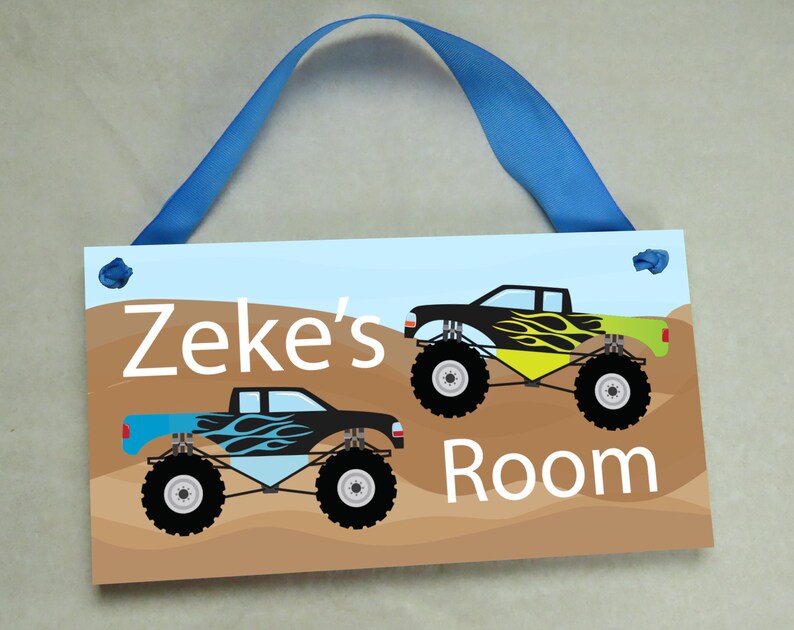 May include: A blue and brown wooden door sign with the text "Zeke's Room" and two monster truck illustrations. The trucks are black with yellow and blue flames.