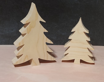 May include: Two wooden Christmas tree ornaments, one larger than the other, on a pink surface. Both trees are made of light brown wood and have a simple, classic design.
