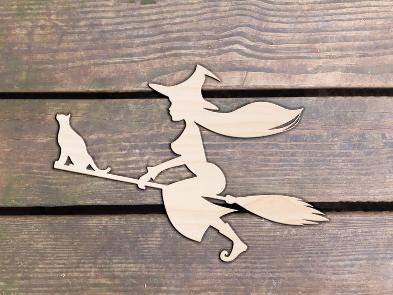 Op de afbeelding: Een houten uitsnijding van een heks die op een bezem rijdt met een kat die op de handgreep zit. De heks draagt een puntige hoed en heeft lang, golvend haar. De uitsnijding is lichtbruin.