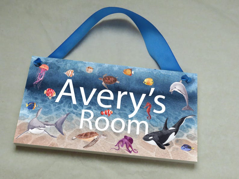 May include: A blue and white wooden door sign with a watercolor ocean scene. The sign says "Avery's Room" and features sea creatures like a shark, dolphin, seahorse, and octopus.