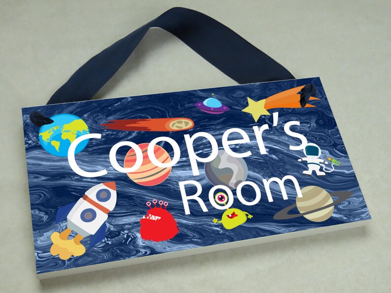May include: A blue and white wooden door sign with the text "Cooper's Room" in white. The sign features a space theme with planets, stars, a rocket, and aliens.