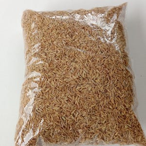 Peut inclure: Un sac en plastique transparent rempli de balles de riz allongées de couleur brun clair. Le contenu se compose de nombreuses balles sèches, texturées et individuelles, tassées dans l'emballage transparent, présentant une teinte beige uniforme.