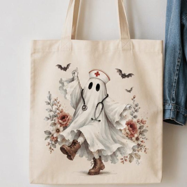May include: A beige canvas tote bag featuring a graphic of a ghost dressed as a nurse, wearing a white cap with a red cross, a stethoscope, and brown boots. The ghost is surrounded by floral arrangements and small flying bats in a soft color palette.