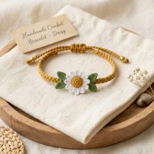 May include: A mustard yellow braided crochet bracelet featuring a central white daisy flower with a yellow center and two green leaves. The bracelet has an adjustable sliding knot closure with small gold-toned beads and a tag reading Handmade Crochet Bracelet - Daisy.