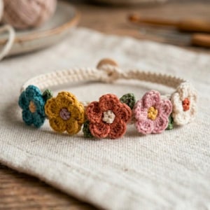 May include: A cream-colored crochet bracelet adorned with five colorful crochet flowers. The flowers are in shades of teal, yellow, orange, pink, and white, each with a contrasting center. The bracelet is handmade and features a wooden button closure.
