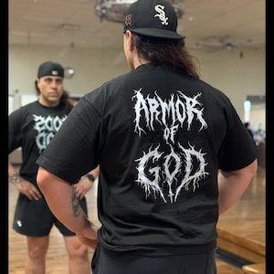 Puede incluir: Camiseta negra con las palabras "ARMOR OF GOD" en una fuente gótica blanca. La persona de la imagen lleva una gorra de béisbol negra con un logotipo blanco. La imagen está tomada frente a un espejo.