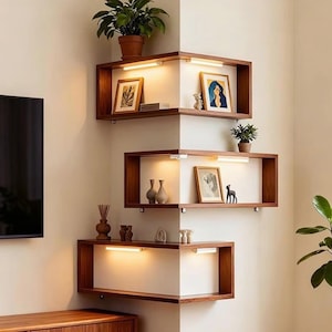 May include: Three tiered wooden corner shelves mounted on a wall, each featuring integrated warm LED lighting. The shelves hold various decorative items including framed pictures, small potted plants, and ceramic vases, creating a display.
