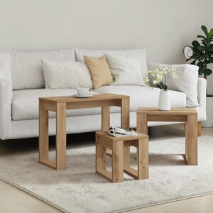 May include: A set of three light brown wooden nesting tables with a rectangular top and open frame legs. The tables are arranged in a cascading formation, with a white ceramic cup on the largest table and a white vase with flowers on the medium table.
