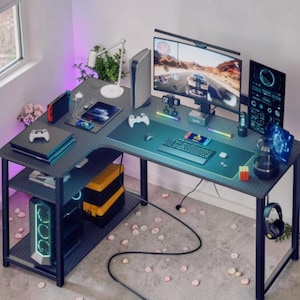 Puede incluir: Un escritorio de juego en forma de L con una superficie oscura texturizada, que incluye un monitor de computadora, una consola vertical, teclado, ratón, auriculares para juegos y varios accesorios electrónicos. Incluye estantes de almacenamiento.