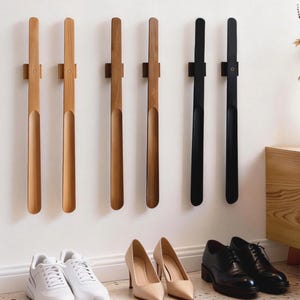 May include: Six long, slender shoehorns mounted vertically on a wall. Four shoehorns are made of light to medium-toned wood, and two are matte black. Each features a curved scoop at the bottom and a small circular detail near the top mount.