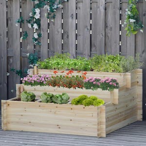 May include: A three-tiered wooden planter box featuring a natural light wood grain finish. The planter is filled with various green leafy vegetables, including heads of lettuce, and clusters of small pink and orange flowering plants.