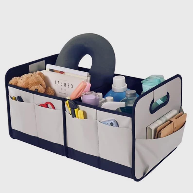 May include: A car organiser in grey, navy blue, and white, with multiple compartments and handles. The organiser is filled with items such as a teddy bear, books, and bottles. Measurements are in centimetres.