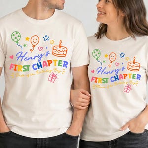 May include: Two off-white t-shirts featuring colorful graphics of balloons, a birthday cake, and a gift box. The text reads Henry's FIRST CHAPTER, with one shirt stating Dada of the Birthday Boy and the other Mama of the Birthday Boy in script.