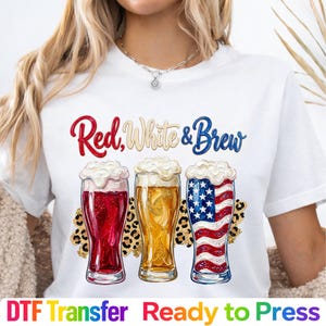 May include: White t-shirt with the text "Red, White & Brew" above three beer glasses. The glasses are filled with red, yellow, and blue-and-white beer, with foam on top. The words "DTF Transfer Ready to Press" are at the bottom.