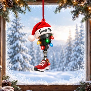 May include: A prosthetic leg ornament featuring a red Santa hat with the word Sweetie printed on the white brim. The prosthetic limb is wrapped in colorful Christmas lights and attached to a red sneaker with a small cluster of red ornaments.