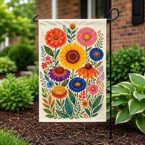 Può includere: Una bandiera da giardino rettangolare con una vivace illustrazione floreale multicolore su sfondo color crema. Il design presenta un grande girasole centrale circondato da vari fiori nelle tonalità dell'arancione, rosa, viola, blu e giallo.
