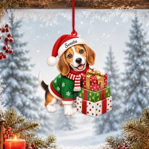 May include: A hanging ornament featuring a beagle puppy wearing a red Santa hat with the text Sweetie, a green jumper with white snowflakes, and a red and white striped scarf. The puppy is holding a stack of three colourful Christmas gift boxes.