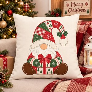 May include: A square throw pillow featuring a graphic of a gnome wearing a red and green patchwork hat with snowflakes and holly. The gnome has a white beard, brown boots, and is holding a gift box decorated with green pine trees.