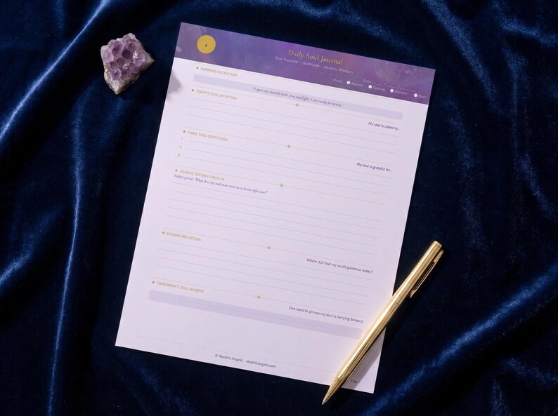 Pode incluir: Um Daily Soul Journal em uma superf&iacute;cie de veludo azul escuro, com uma caneta dourada e um cristal roxo. O di&aacute;rio tem um cabe&ccedil;alho roxo e branco com o t&iacute;tulo "Daily Soul Journal". O di&aacute;rio tem prompts para reflex&atilde;o.