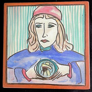 Könnte beinhalten: Eine quadratische Keramikfliese mit einer handgemalten Illustration einer Person mit langem Haar, die eine rosa Mütze und ein blaues Kleidungsstück trägt. Die Person hält ein kleines kreisförmiges Objekt mit einer zentralen Figur. Hintergrund mit türkisen Streifen.