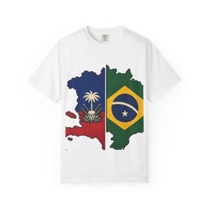 Puede incluir: Una camiseta blanca de manga corta con un diseño gráfico dividido en la parte delantera. El lado izquierdo muestra el mapa de Haití con la bandera haitiana, mientras que el lado derecho muestra el mapa de Brasil con la bandera brasileña.