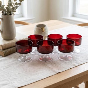 Peut inclure: Un ensemble de six petits bols à dessert ronds en verre rouge profond, chacun doté d'une courte base en verre transparent. Les bols sont disposés en groupe, mettant en valeur leur couleur cramoisie vive et leur structure en verre lisse.