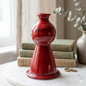 May include: A glossy, deep red ceramic vase with a distinct hourglass silhouette, featuring a wide, flared base that tapers into a rounded midsection and a narrow neck with a small, circular opening at the top, showcasing a smooth, reflective finish.