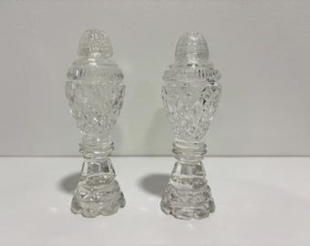 May include: A pair of clear glass salt and pepper shakers featuring a faceted diamond-cut pattern on the body, a rounded top with horizontal ridges, and a wide, scalloped base. The glass is transparent with a reflective, polished finish.