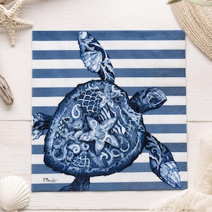 May include: A square paper napkin featuring a blue and white horizontal striped background with a central illustration of a sea turtle. The turtle shell is decorated with intricate blue and white patterns, including a prominent starfish design.