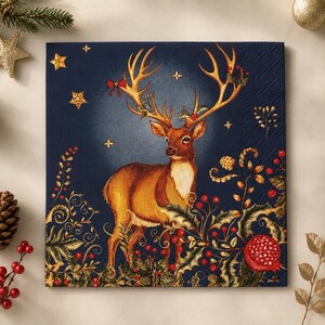 May include: A square paper napkin featuring a dark navy blue background with a central illustration of a brown deer with large antlers. The deer is surrounded by red berries, green holly leaves, a pomegranate, and small gold stars.