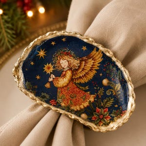 May include: A decorative oyster shell napkin ring featuring a painted illustration of an angel with golden wings and a patterned dress against a dark blue starry background with holly and poinsettia accents, finished with a gold-painted scalloped edge.