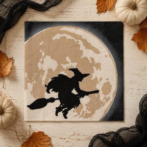 May include: A square paper napkin featuring a black silhouette of a witch flying on a broomstick against a large, textured beige full moon. The background surrounding the moon is solid black, creating a high-contrast graphic design.