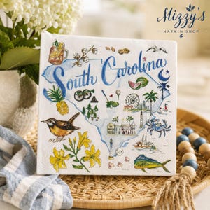May include: A white paper napkin featuring a blue watercolor map of South Carolina with the text South Carolina in blue script. Illustrations include a pineapple, a bird, yellow flowers, a crab, a fish, a lighthouse, and a Ferris wheel.
