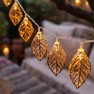May include: A decorative string of warm white LED lights, each shaped like a golden leaf. The leaf lights are strung on a clear wire. The lights are suitable for indoor or outdoor use, creating a warm and inviting atmosphere.
