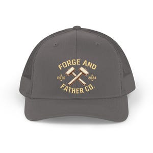 May include: A gray trucker hat with a mesh back and a curved brim. The front of the hat features the text "FORGE AND FATHER CO." in a tan color, along with crossed hammers and the year "2024". The hat has a classic, casual style.