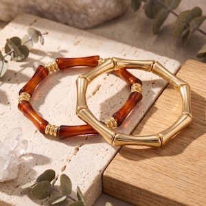 Peut inclure: Deux bracelets circulaires au design inspiré du bambou. L'un est fabriqué en métal doré poli, tandis que l'autre alterne entre des segments en résine couleur ambre lisse et de petites entretoises en métal doré à motifs côtelés.