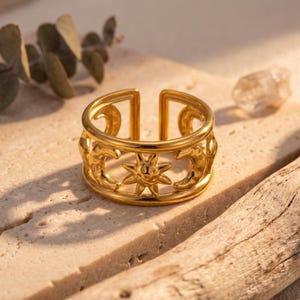 May include: A gold-toned open band ring featuring a repeating cutout design of suns and crescent moons. The metal surface has a polished finish, and the band is constructed with two parallel circular rails connected by the celestial motifs.