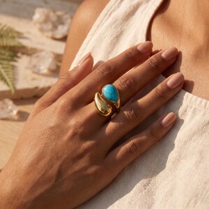 Peut inclure: Bague dorée ornée d'une pierre turquoise en forme de goutte d'eau. La bague présente un design ouvert unique avec une finition lisse et polie. Un bijou élégant.