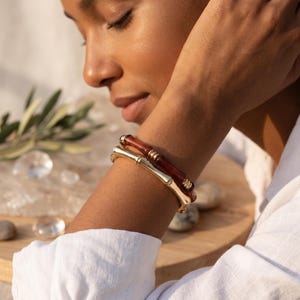 Peut inclure: Deux bracelets superposés au design inspiré du bambou. L'un est fabriqué en métal doré poli, tandis que l'autre est composé d'une résine translucide de couleur ambre profond. Les deux pièces présentent des maillons cylindriques segmentés.