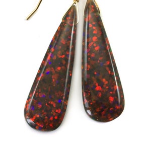 May include: A pair of teardrop-shaped earrings with a red, black, and green opal stone. The earrings are made with gold-toned metal.