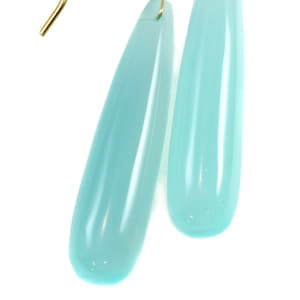 May include: A pair of gold dangle earrings with teardrop-shaped light blue gemstone pendants.