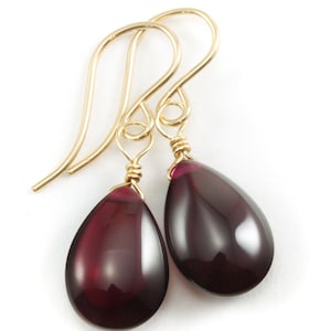 May include: A pair of gold dangle earrings with teardrop-shaped red gemstones.