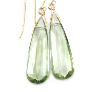 May include: A pair of gold dangle earrings with light green teardrop-shaped gemstones.