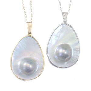 Peut inclure: Deux pendentifs de forme ovale avec une grosse perle à l'intérieur. Un pendentif est sur une chaîne en or et l'autre sur une chaîne en argent.
