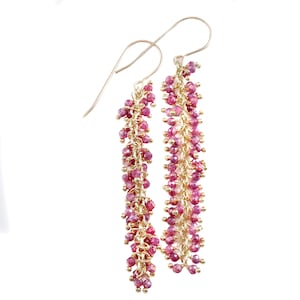 Op de afbeelding: Een paar lange, hangende oorbellen met een gouden ketting en roze robijn kralen. De oorbellen zijn gemaakt van goud en roze robijn kralen.