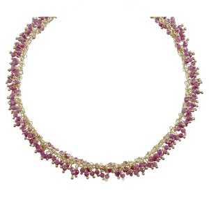 May include: A gold chain necklace with pink beads. The beads are clustered together in a cascading design.